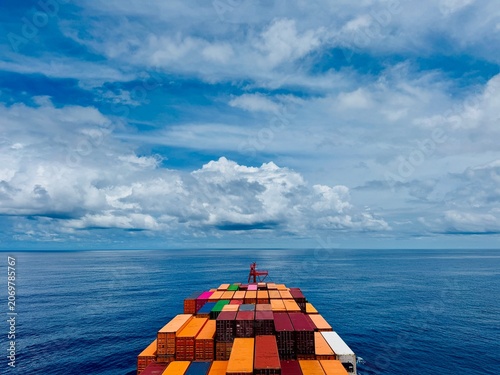 Konstfotografi Colorful cargo containers stacked on the deck of a container ship sailing across a calm ocean beneath dramatic clouds