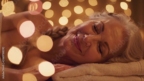 Senior woman with eyes closed relaxing at a luxury spa with warm golden lights