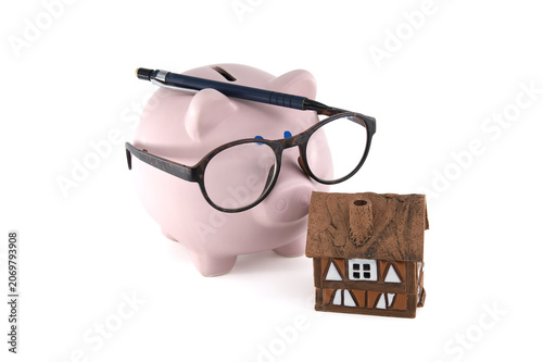 Piggy bank with glasses and pen next to a miniature house, symbolizing savings for home ownership