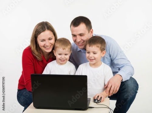A happy family with two young children learning together on a laptop computer, parents watching with smiles
