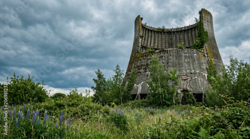 Abandoned concrete structure overgrown with vegetation under cloudy sky  