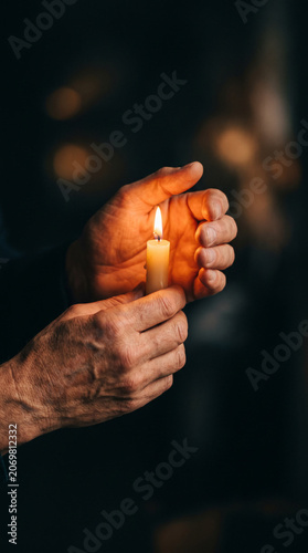 Hands holding a burning candle in low light setting  