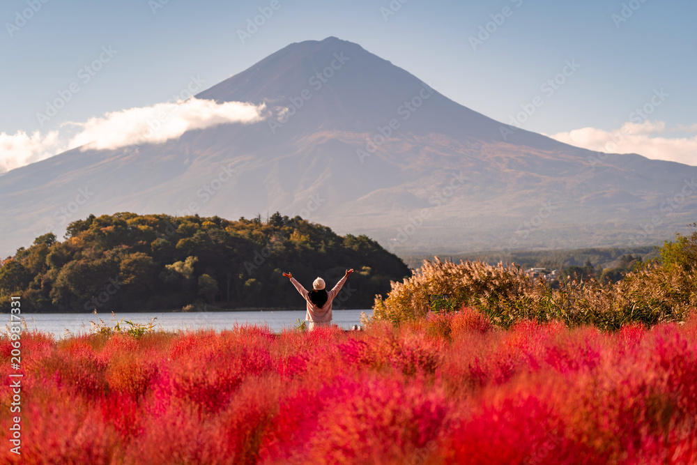 Fototapeta premium Joyful tourist woman in a vibrant red kochia field enjoying the scenic landscape of Mount Fuji and Lake Kawaguchiko, Japan