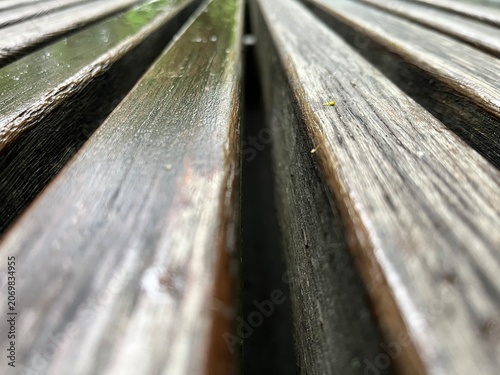 Abstract dark wood texture background with parallel line pattern. Wood bench after rain in a park. Lines of a macro wood bench with water.
