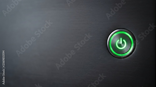 Glowing green power button on black brushed metal surface