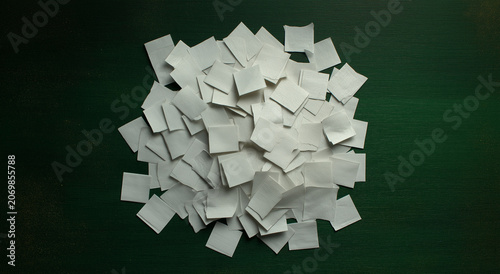 a collection of plain white square papers, each with slightly rough or torn edges, is strewn across a dark pink wood surface