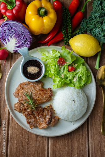 Healthy balanced meal concept. Roasted pork with rice, salad, and colorful raw ingredients like bell pepper, kale, and chili around the plate.