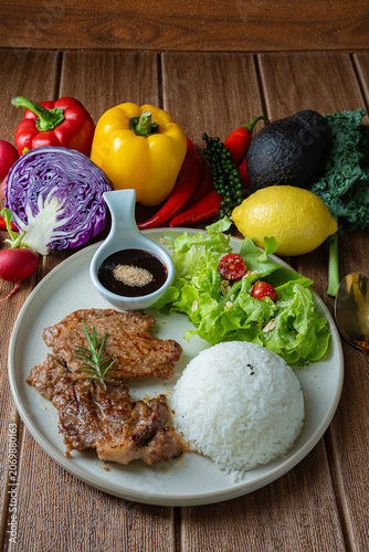 Healthy balanced meal concept. Roasted pork with rice, salad, and colorful raw ingredients like bell pepper, kale, and chili around the plate.