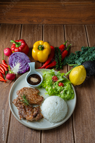 Healthy balanced meal concept. Roasted pork with rice, salad, and colorful raw ingredients like bell pepper, kale, and chili around the plate.