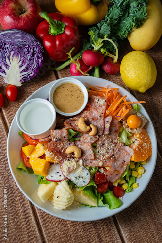 Fresh mixed vegetable and fruit salad bowl with crispy bacon, sesame dressing, and colorful ingredients on wooden background.