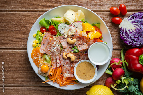 Fresh mixed vegetable and fruit salad bowl with crispy bacon, sesame dressing, and colorful ingredients on wooden background.