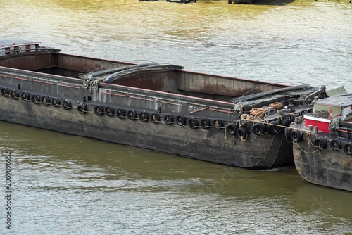 фотографія Two large barges are moored together on a murky river, ready for transport