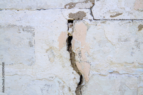 Large crack in an old weathered white brick wall. Structural damage and decay concept. Background for construction repair or renovation project.