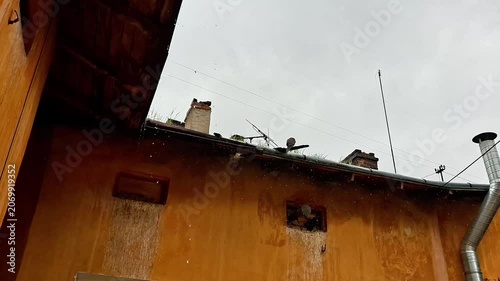 Rainwater Cascading from Rooftop During Heavy Downpour. Exterior building wall and roof gutters under intense rainfall, showcasing wet urban architecture and stormy weather conditions
