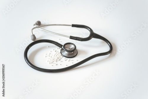 Fotografie Black medical stethoscope over small white homeopathic pills on bright background evoking alternative medicine, holistic healthcare, and natural treatment marketing concepts
