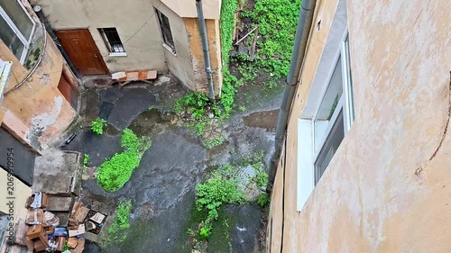 Rainy urban courtyard framed by historic residential buildings and lush greenery. Wet surfaces, soft rainfall, and a peaceful atmosphere capture everyday city life in rainy weather
