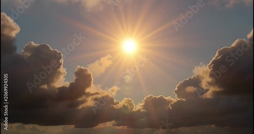 Bright sun shining above fluffy clouds in clear blue sky

