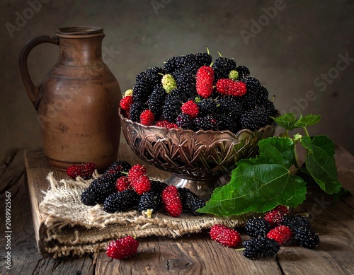 A still life of mulberries, both black and red, piled in a silver bowl next to an earthen jug
