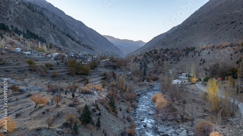 Aerial view of Astore Valley with a winding river, terraced fields, and a small village nestled among autumn-colored trees in the mountainous landscape of Astore, Gilgit, Pakistan.