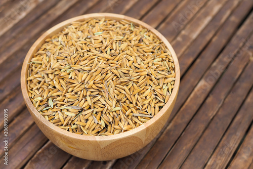Golden paddy rice grains in a wooden bowl on bamboo wooden table background.