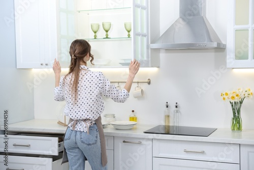 Bild auf Leinwand Woman opening cabinet with clean glasses in kitchen, back view