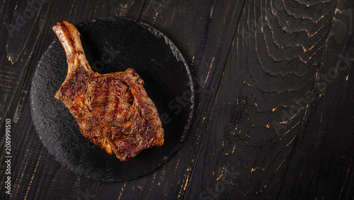 Tomahawk steak on black slate plate over rustic wooden table with copy space