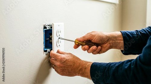 Close-up of a person securing a newly installed white dual electrical outlet on a plain wall with a screwdriver.