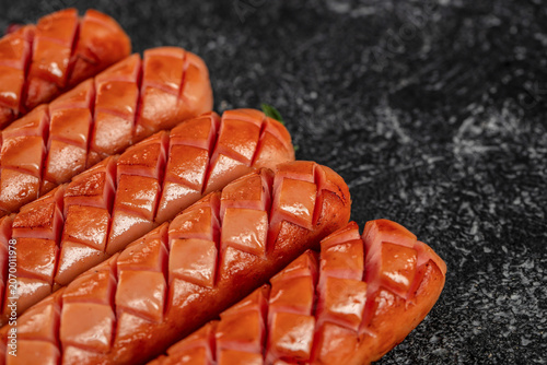 Fotografía Grilled sausages with diagonal cuts on dark textured background