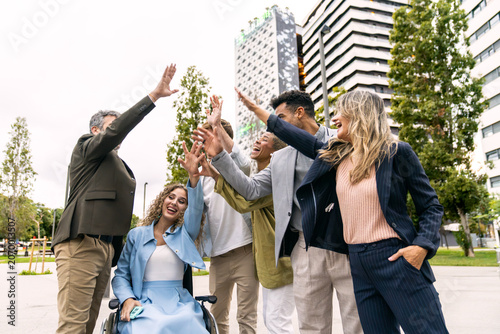 Diverse business people high fiving, celebrating teamwork, success, and inclusion in a city park with office buildings