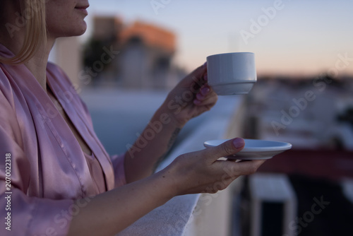 Obraz na plátně Woman enjoying quiet morning ritual, holding espresso cup and saucer on balcony