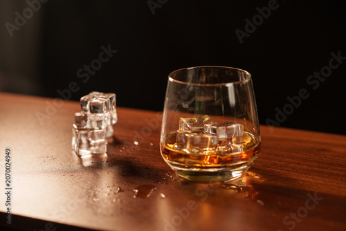 Elegant Whiskey Glass with Ice Cubes on Dark Wooden Table in Warm Mood Lighting