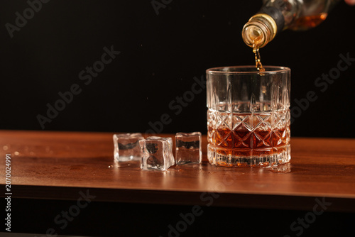 Pouring Whiskey into a Glass with Ice on a Vintage Wooden Surface