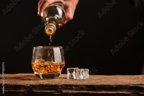 Pouring Whiskey into a Glass with Ice on a Vintage Wooden Surface