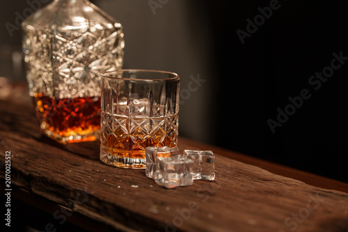 Crystal Decanter and Matching Cut Glass with Amber Whiskey and Ice Cubes on Rustic Wood Surface