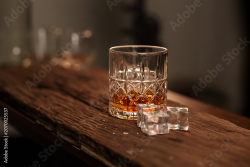 Crystal Cut Whiskey Glass with Amber Liquor and Ice Cubes on Rustic Vintage Wood Surface