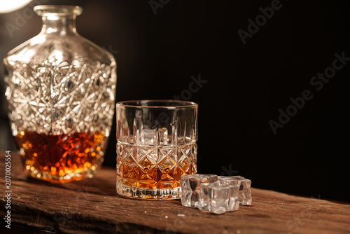 A glass liquor bottle and whiskey with ice on a wooden table.
