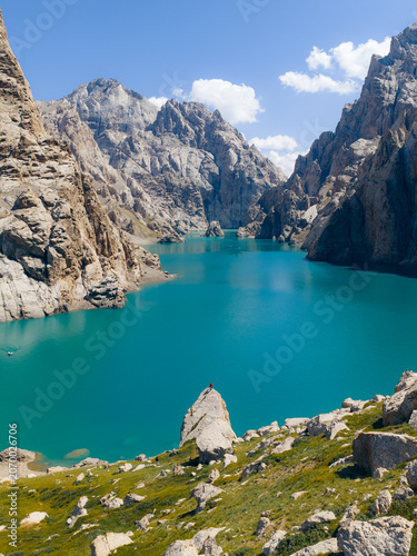 Aerial view of the turquoise waters of Kol-Suu lake surrounded by steep rocky cliffs and jagged mountain peaks in At-Bashi District, Naryn Region, Kyrgyzstan.