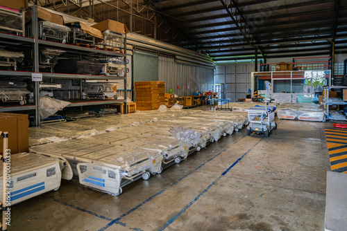 Large warehouse interior storing wrapped medical beds and hospital equipment on industrial shelving under a high metal roof.