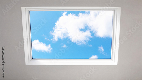 Rectangular sunroof framing moving clouds against a blue sky, minimalist architectural detail.