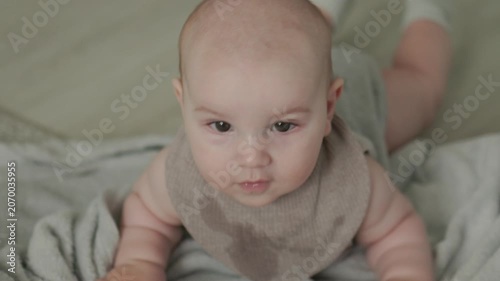 Teething baby lying down, chewing toy and moving hands and feet actively. Top view of sweet infant crying and smiling during first teeth growth milestone. Pediatric and parenting concept.