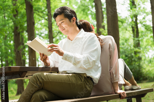 公園のベンチで読書を楽しむ40代夫婦