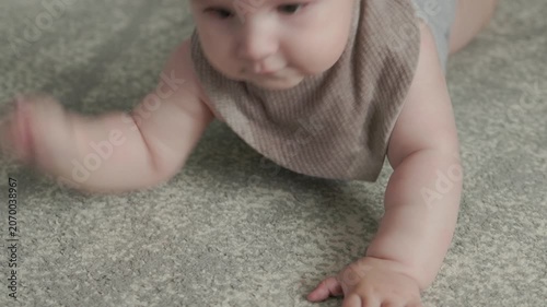 Teething baby lying down, chewing toy and moving hands and feet actively. Top view of sweet infant crying and smiling during first teeth growth milestone. Pediatric and parenting concept.
