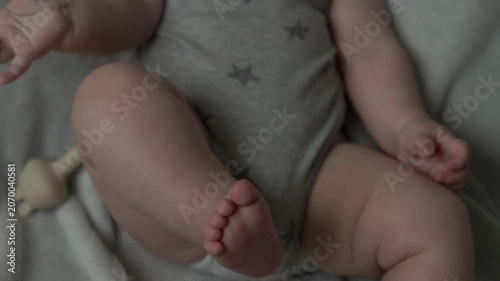Teething baby lying down, chewing toy and moving hands and feet actively. Top view of sweet infant crying and smiling during first teeth growth milestone. Pediatric and parenting concept.