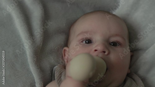 Teething baby lying down, chewing toy and moving hands and feet actively. Top view of sweet infant crying and smiling during first teeth growth milestone. Pediatric and parenting concept.