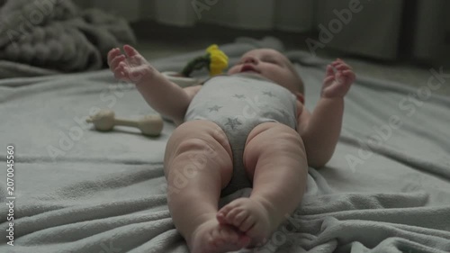 Teething baby lying down, chewing toy and moving hands and feet actively. Top view of sweet infant crying and smiling during first teeth growth milestone. Pediatric and parenting concept.