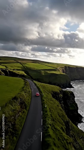 Small red car on dramatic coastal road above ocean.