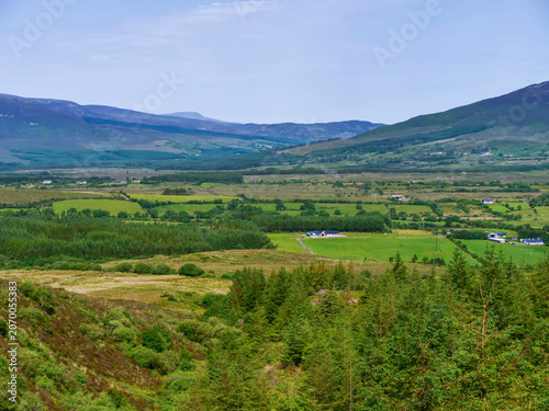 Green fields and forest and mountains in the background. View from The Windy Gap view point. Ireland. Irish nature scenery. Blue sky.