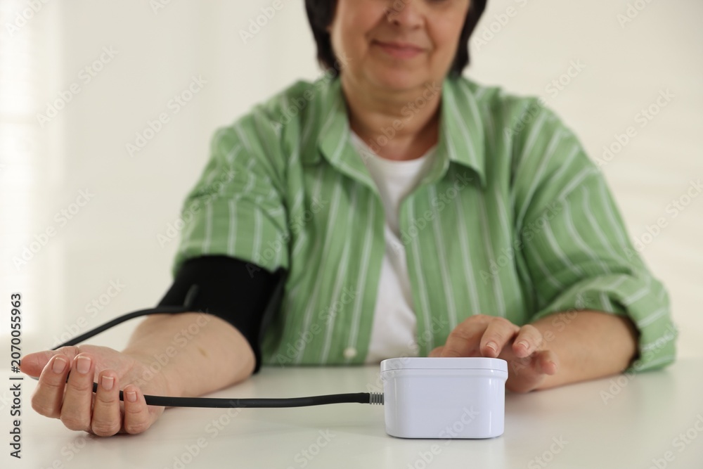 Fototapeta premium Woman measuring blood pressure with sphygmomanometer at table indoors, closeup