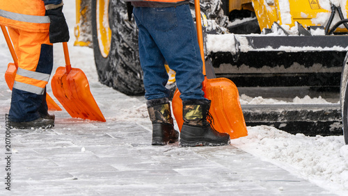 Cuadro en lienzo Worker shovels snow with orange tools beside heavy machinery