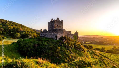 A stone structure crowns a verdant hill, bathed in the golden light of sunset, with distant trees